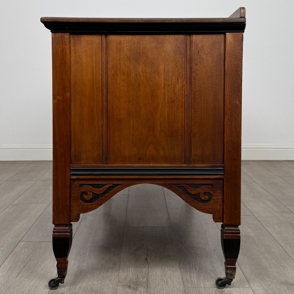 An antique mahogany low sideboard featuring six drawers, a central double cupboard, highly figured veneer panels, brass handles, and turned legs on castors. View IV