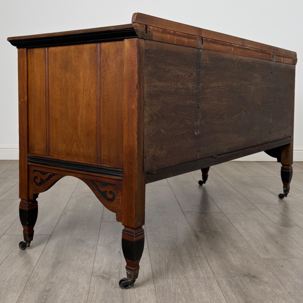 An antique mahogany low sideboard featuring six drawers, a central double cupboard, highly figured veneer panels, brass handles, and turned legs on castors. View V