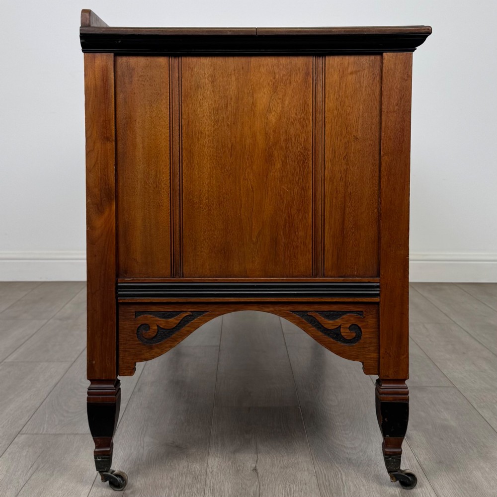 An antique mahogany low sideboard featuring six drawers, a central double cupboard, highly figured veneer panels, brass handles, and turned legs on castors. View VIII