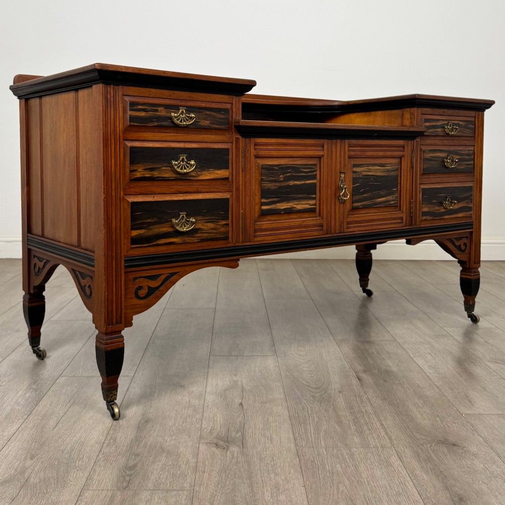 An antique mahogany low sideboard featuring six drawers, a central double cupboard, highly figured veneer panels, brass handles, and turned legs on castors. View IX