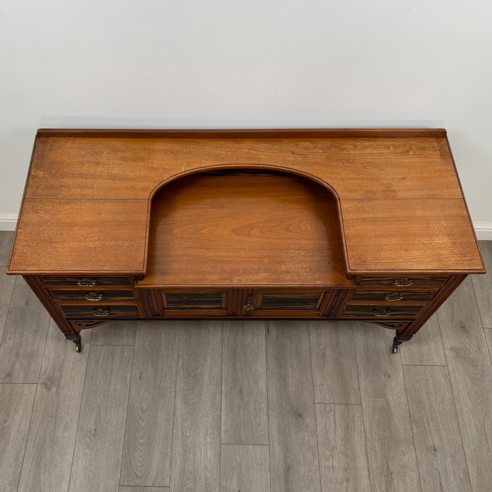 An antique mahogany low sideboard featuring six drawers, a central double cupboard, highly figured veneer panels, brass handles, and turned legs on castors. View X