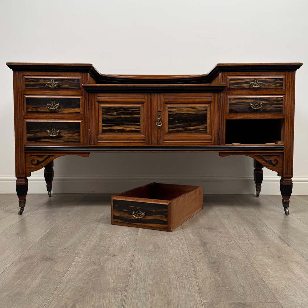 An antique mahogany low sideboard featuring six drawers, a central double cupboard, highly figured veneer panels, brass handles, and turned legs on castors. View XI