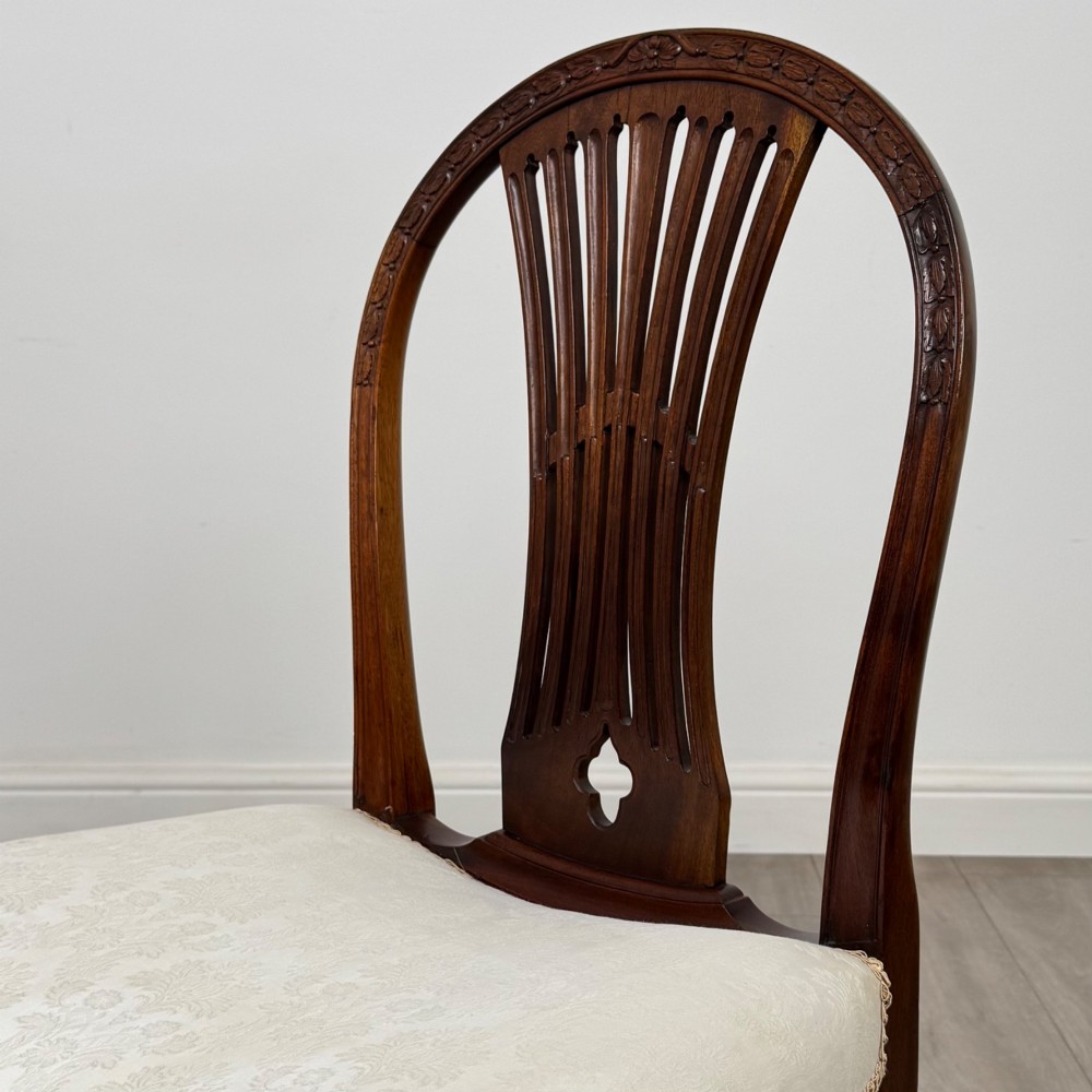 A set of eight 19th-century Hepplewhite style mahogany dining chairs featuring carved openwork back splats, square tapered legs, and light cream upholstered seats. View V