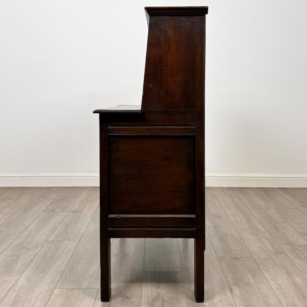A dark brown 19th-century carved oak cupboard featuring an open upper shelf supported by carved pillars, above a lower two-door cabinet with relief-carved panels and iron hinges. View IV