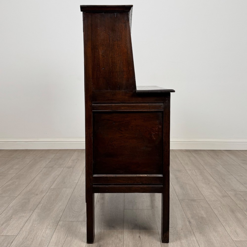A dark brown 19th-century carved oak cupboard featuring an open upper shelf supported by carved pillars, above a lower two-door cabinet with relief-carved panels and iron hinges. View VIII