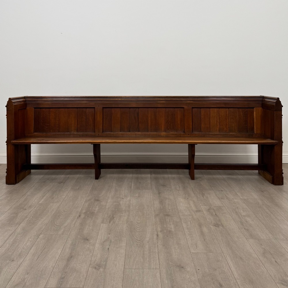 A long nineteenth-century oak church pew featuring a panelled back, moulded end supports, and a single solid wood bench seat.