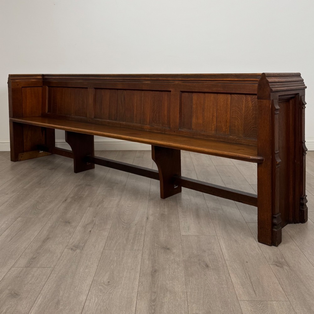 A long nineteenth-century oak church pew featuring a panelled back, moulded end supports, and a single solid wood bench seat. View II