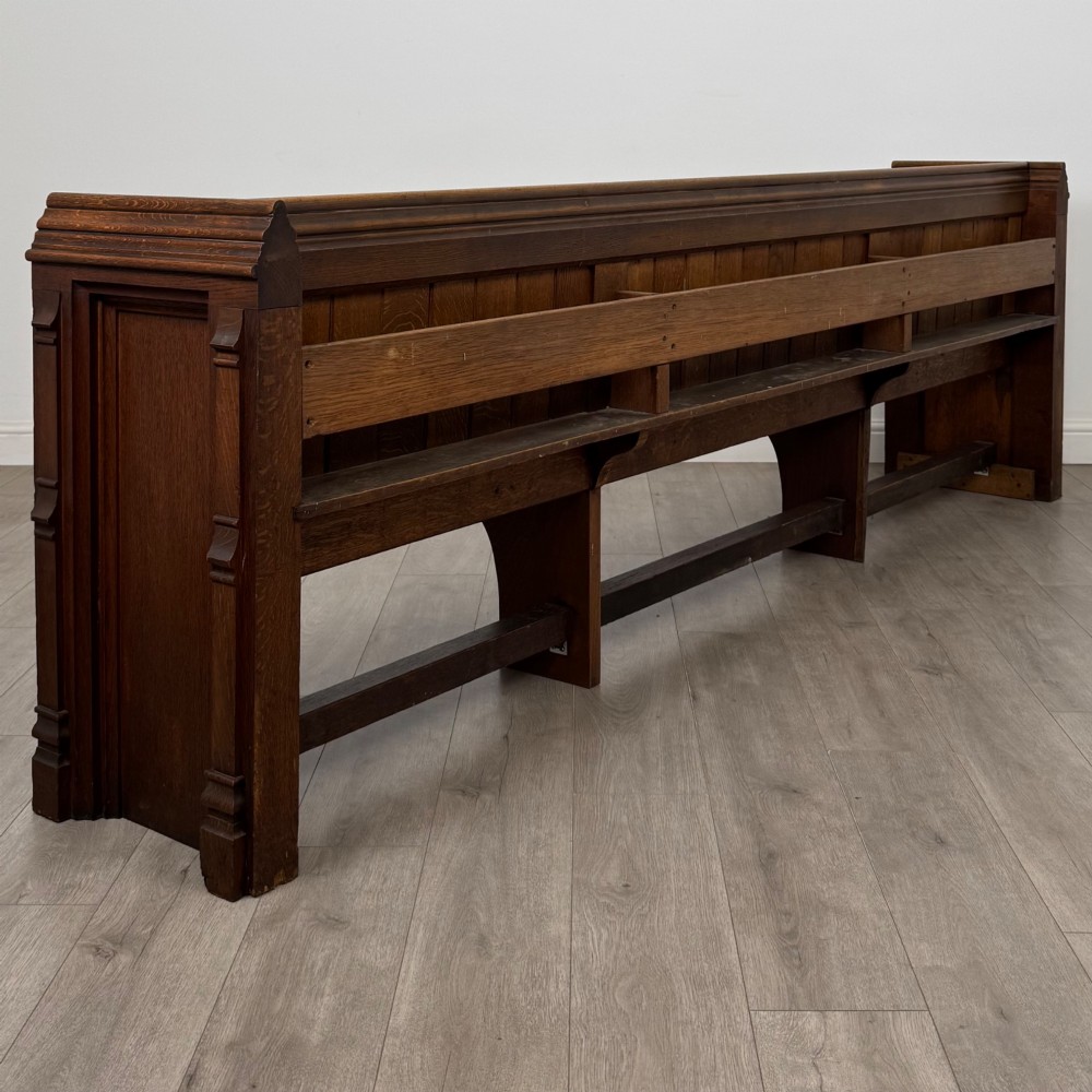 A long nineteenth-century oak church pew featuring a panelled back, moulded end supports, and a single solid wood bench seat. View IV