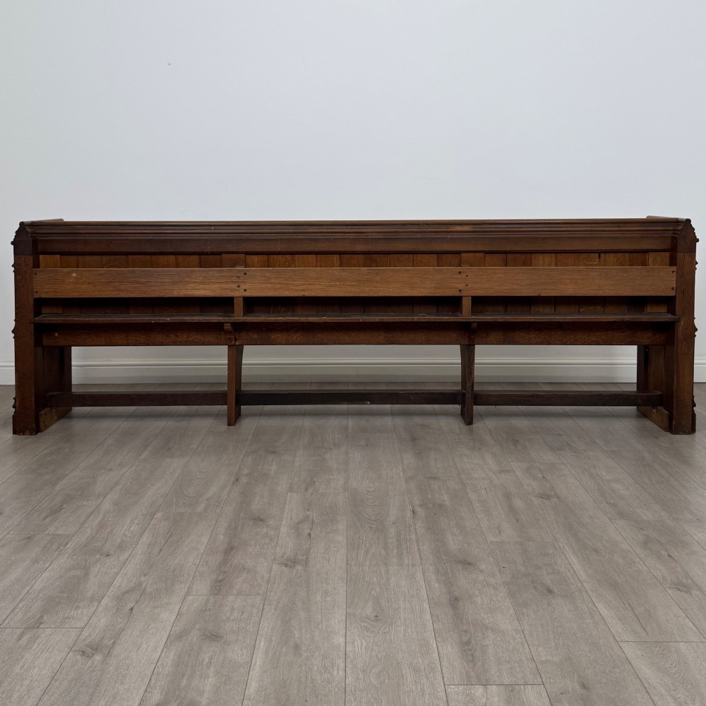 A long nineteenth-century oak church pew featuring a panelled back, moulded end supports, and a single solid wood bench seat. View V
