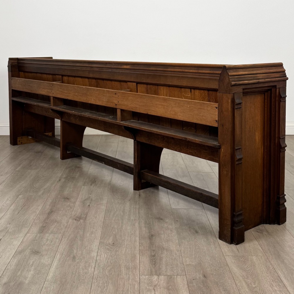 A long nineteenth-century oak church pew featuring a panelled back, moulded end supports, and a single solid wood bench seat. View VI