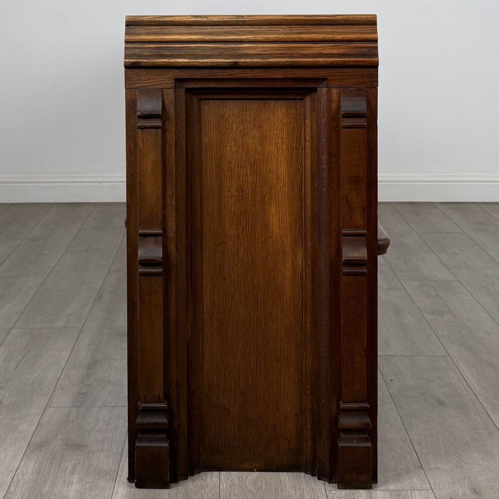 A long nineteenth-century oak church pew featuring a panelled back, moulded end supports, and a single solid wood bench seat. View VII