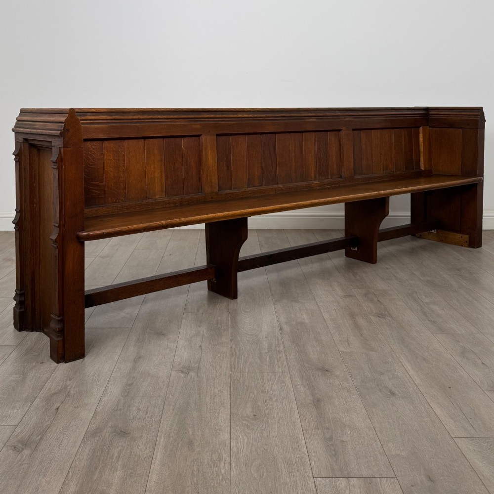 A long nineteenth-century oak church pew featuring a panelled back, moulded end supports, and a single solid wood bench seat. View VIII