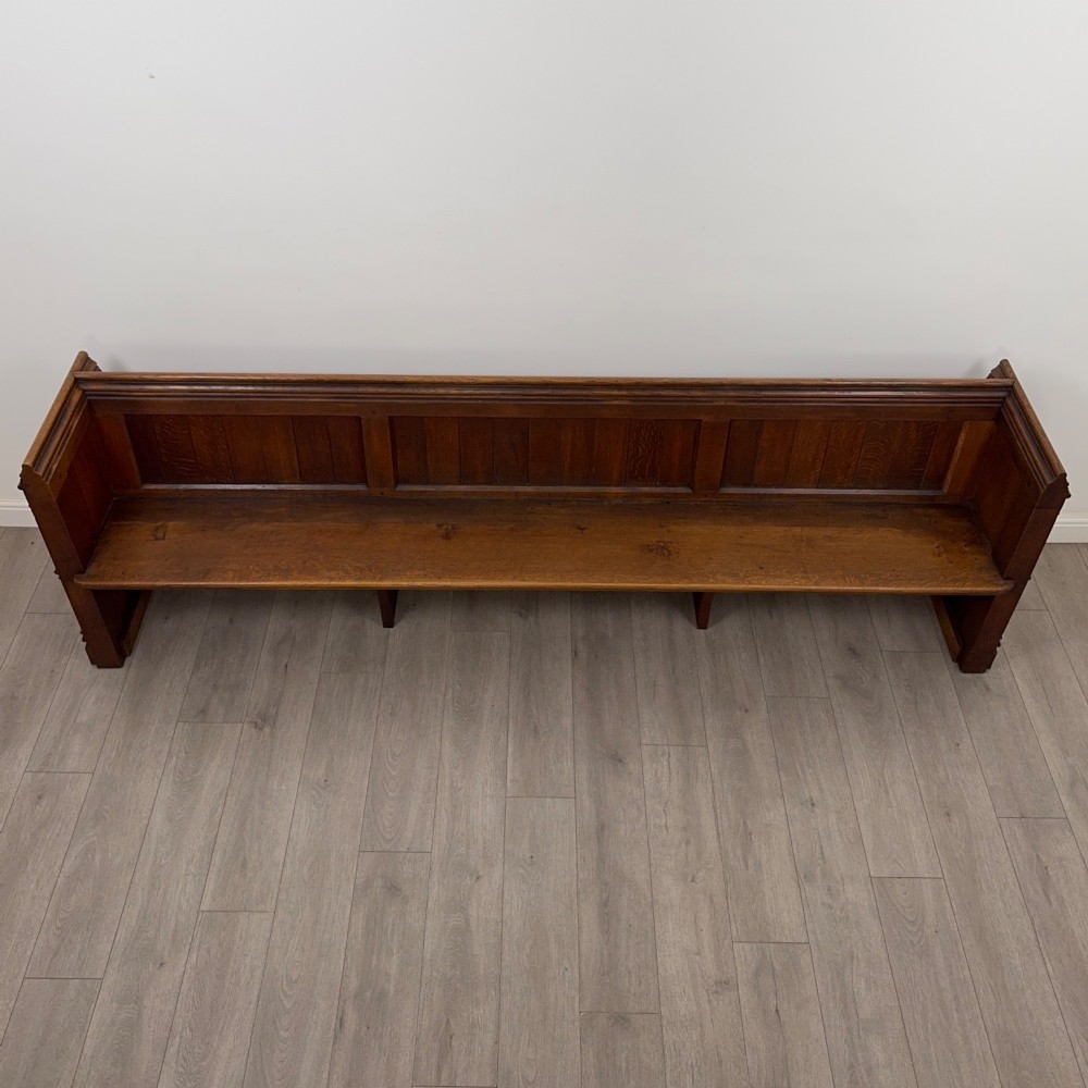 A long nineteenth-century oak church pew featuring a panelled back, moulded end supports, and a single solid wood bench seat. View IX