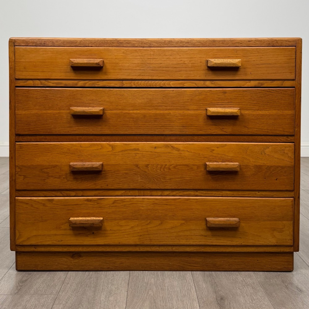 A golden oak chest of four full-width drawers featuring wooden bar handles and a solid plinth base.