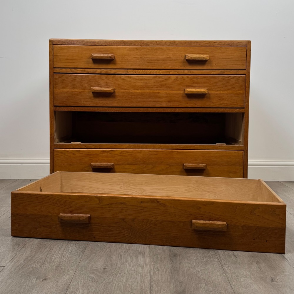 A golden oak chest of four full-width drawers featuring wooden bar handles and a solid plinth base. View X