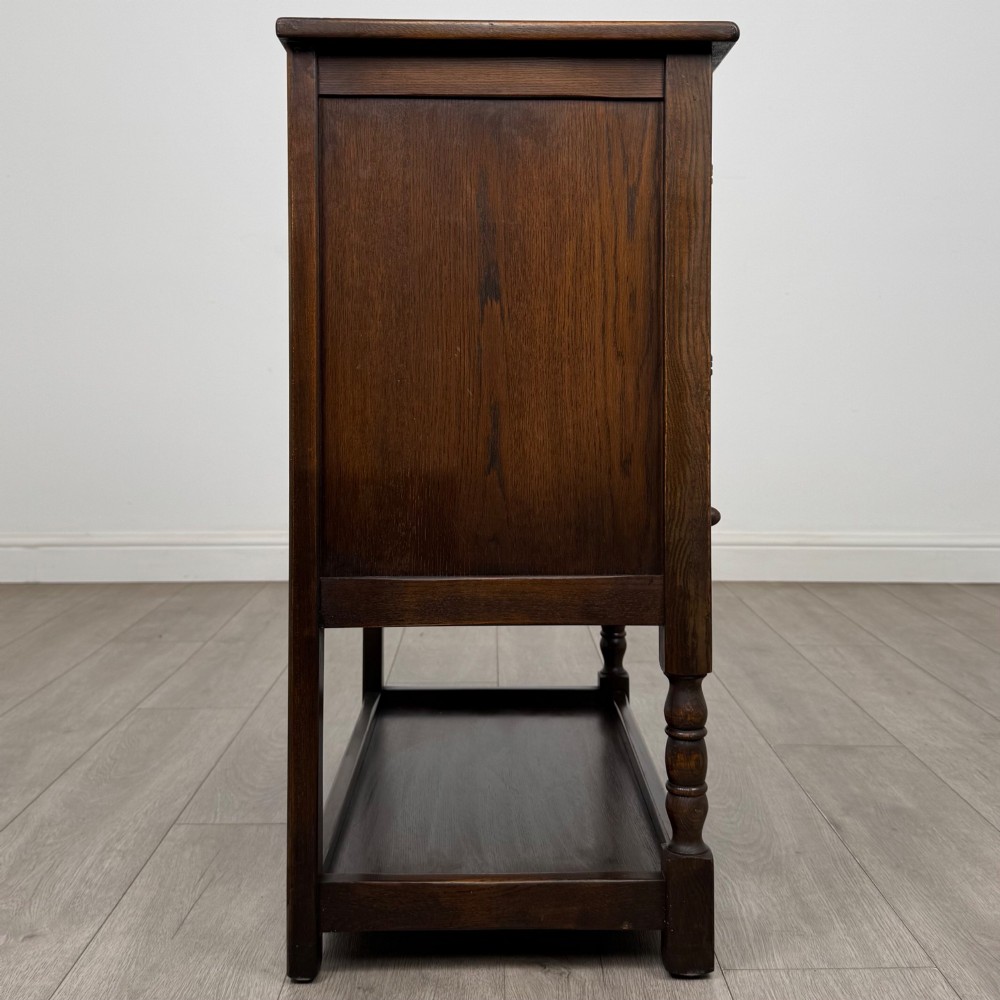 A dark oak cupboard featuring two linenfold carved doors, iron butterfly hinges, a single lower drawer, turned legs, and a bottom shelf. View VIII
