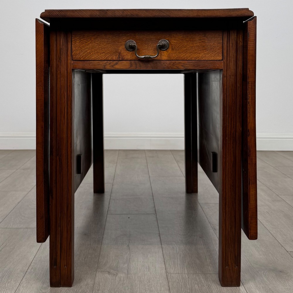 A 20th-century oak drop-leaf table shown with lowered flaps, featuring a single end drawer with a brass drop handle and square legs. View IV