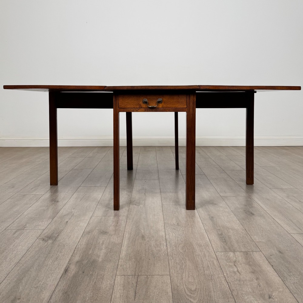 A 20th-century oak drop-leaf table shown with lowered flaps, featuring a single end drawer with a brass drop handle and square legs. View V