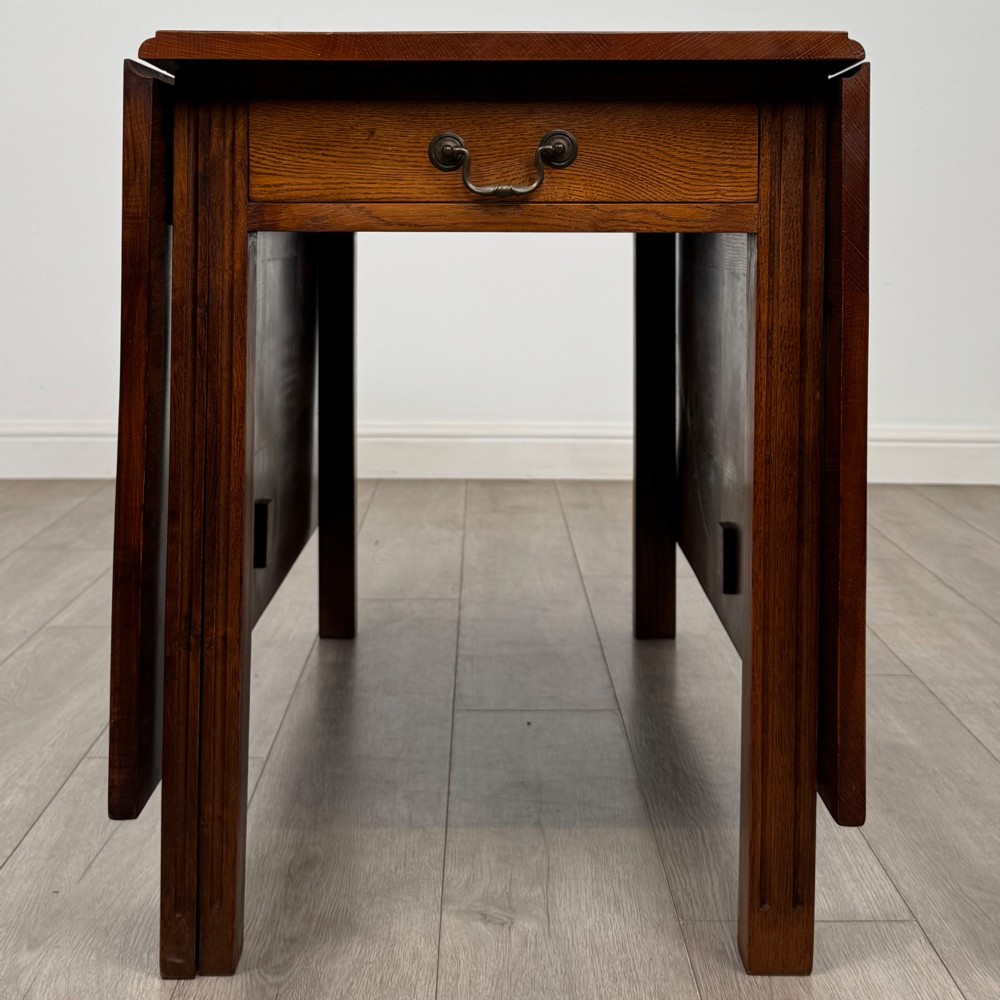 A 20th-century oak drop-leaf table shown with lowered flaps, featuring a single end drawer with a brass drop handle and square legs. View IX