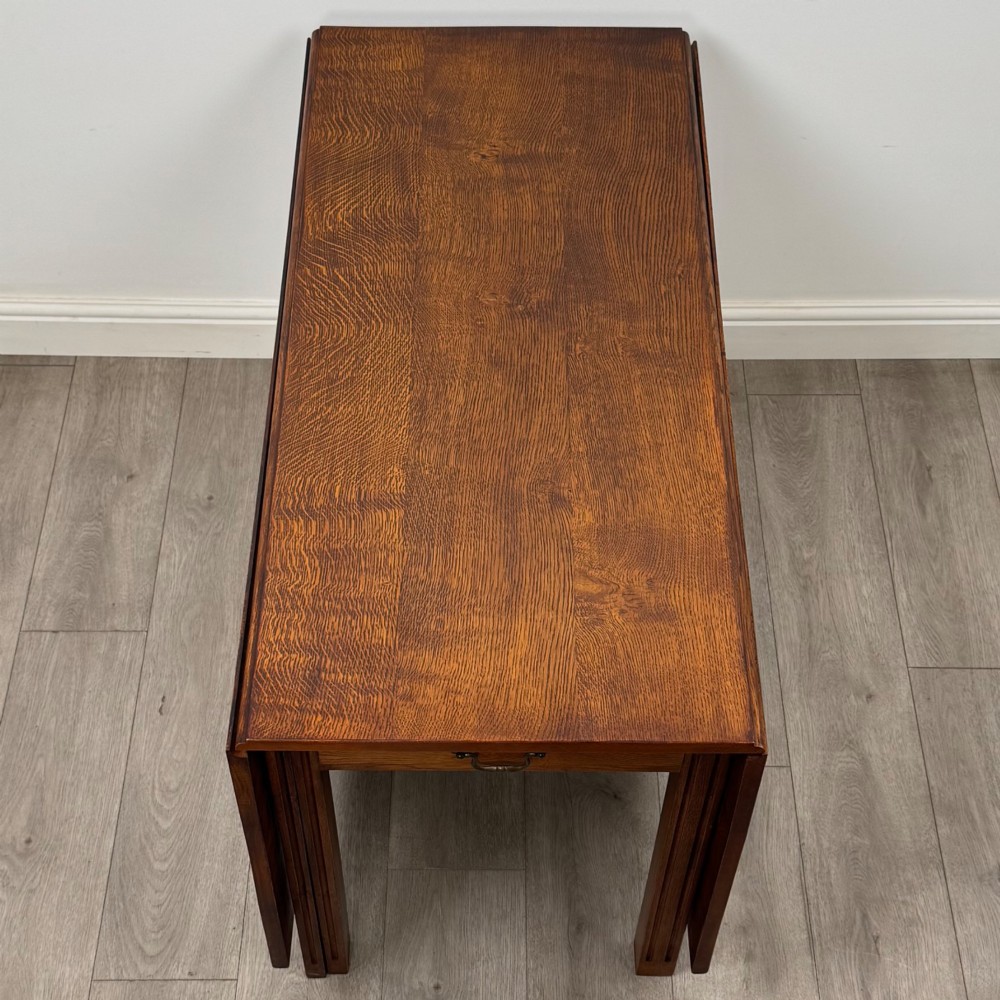 A 20th-century oak drop-leaf table shown with lowered flaps, featuring a single end drawer with a brass drop handle and square legs. View X