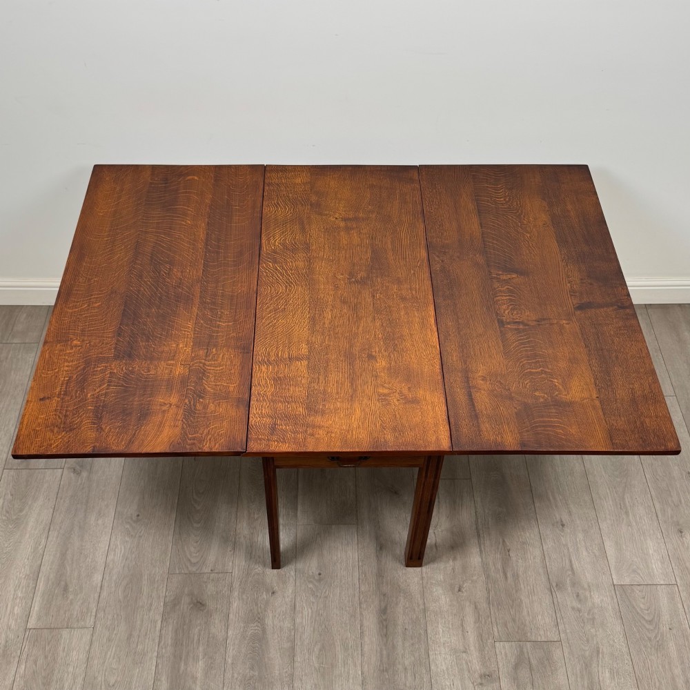 A 20th-century oak drop-leaf table shown with lowered flaps, featuring a single end drawer with a brass drop handle and square legs. View XI
