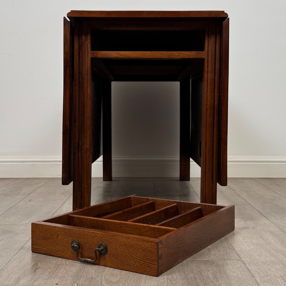 A 20th-century oak drop-leaf table shown with lowered flaps, featuring a single end drawer with a brass drop handle and square legs. View XII