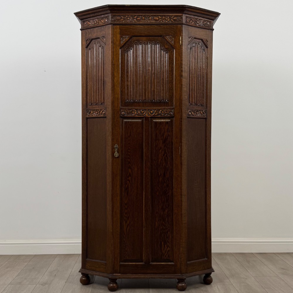 A dark oak wardrobe featuring upper panels carved with a linenfold motif, decorative floral friezes, canted sides, and turned bun feet.