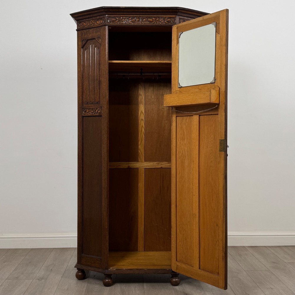 A dark oak wardrobe featuring upper panels carved with a linenfold motif, decorative floral friezes, canted sides, and turned bun feet. View II