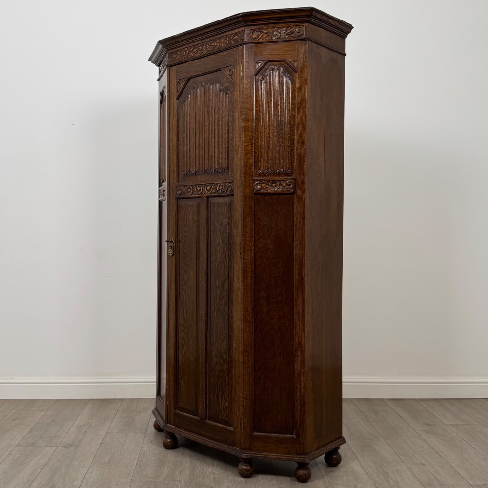 A dark oak wardrobe featuring upper panels carved with a linenfold motif, decorative floral friezes, canted sides, and turned bun feet. View III