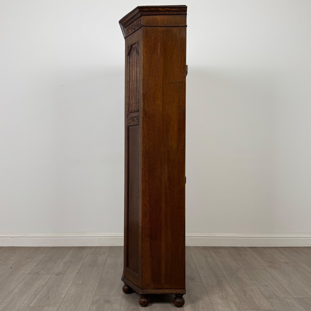 A dark oak wardrobe featuring upper panels carved with a linenfold motif, decorative floral friezes, canted sides, and turned bun feet. View IV