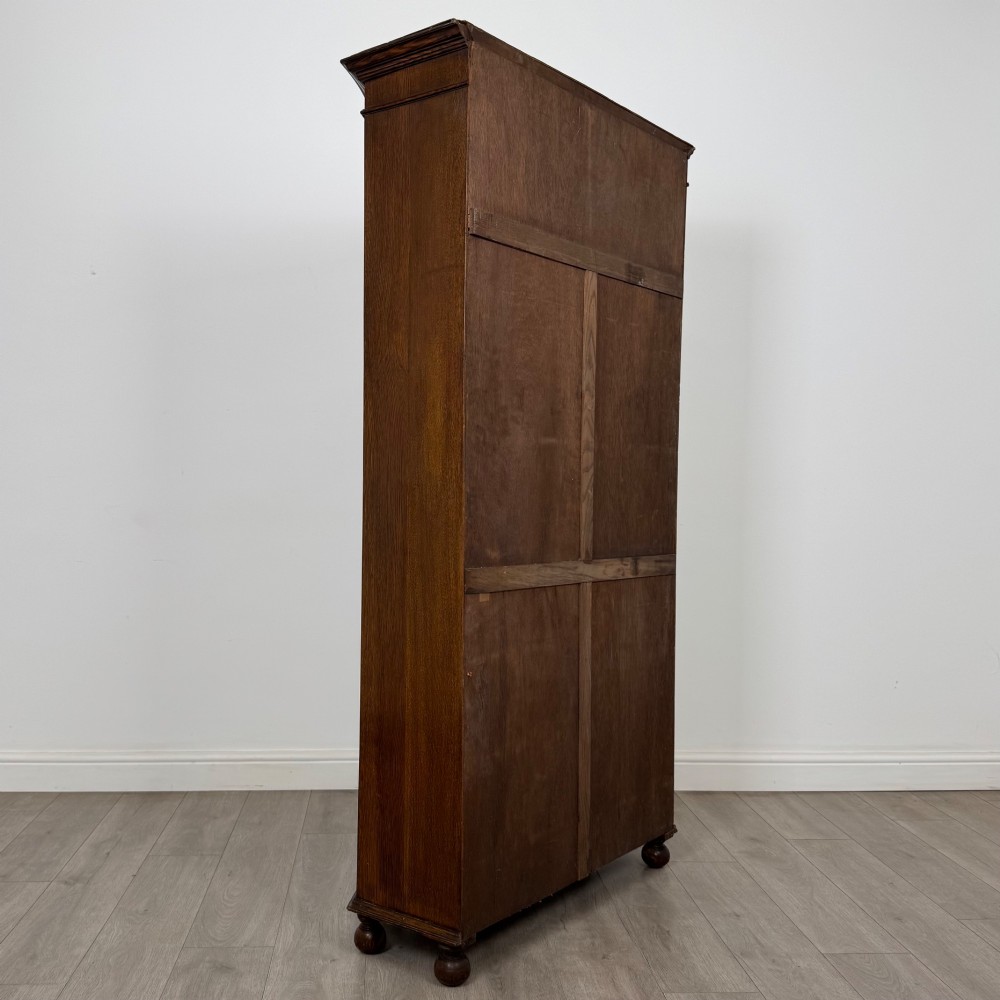 A dark oak wardrobe featuring upper panels carved with a linenfold motif, decorative floral friezes, canted sides, and turned bun feet. View V