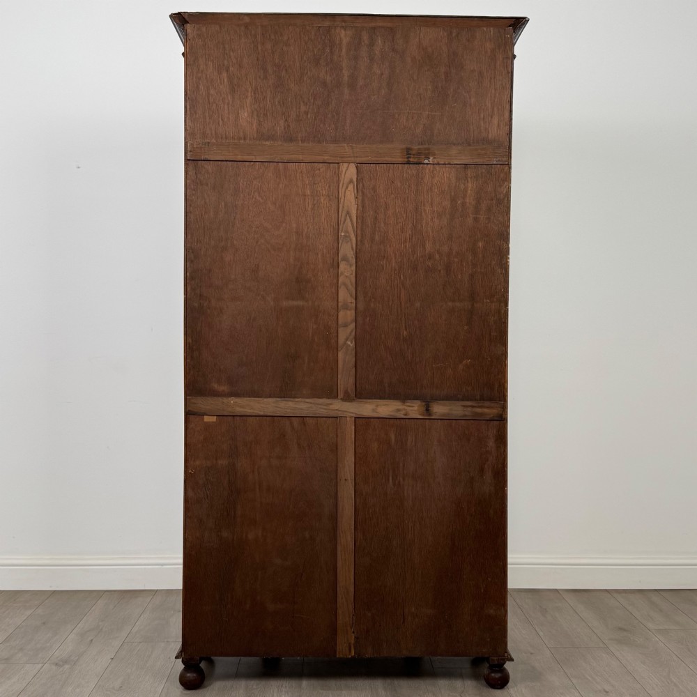 A dark oak wardrobe featuring upper panels carved with a linenfold motif, decorative floral friezes, canted sides, and turned bun feet. View VI