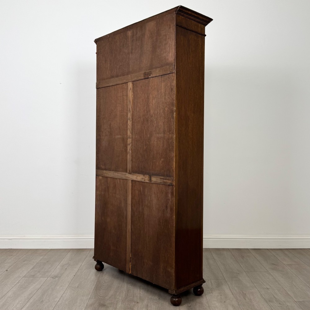 A dark oak wardrobe featuring upper panels carved with a linenfold motif, decorative floral friezes, canted sides, and turned bun feet. View VII