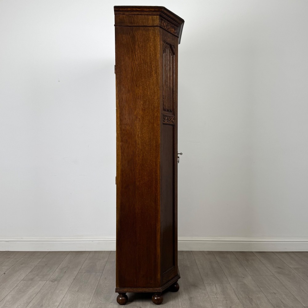 A dark oak wardrobe featuring upper panels carved with a linenfold motif, decorative floral friezes, canted sides, and turned bun feet. View VIII