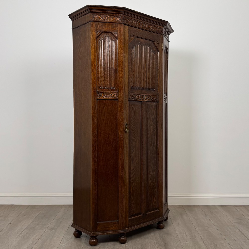 A dark oak wardrobe featuring upper panels carved with a linenfold motif, decorative floral friezes, canted sides, and turned bun feet. View IX