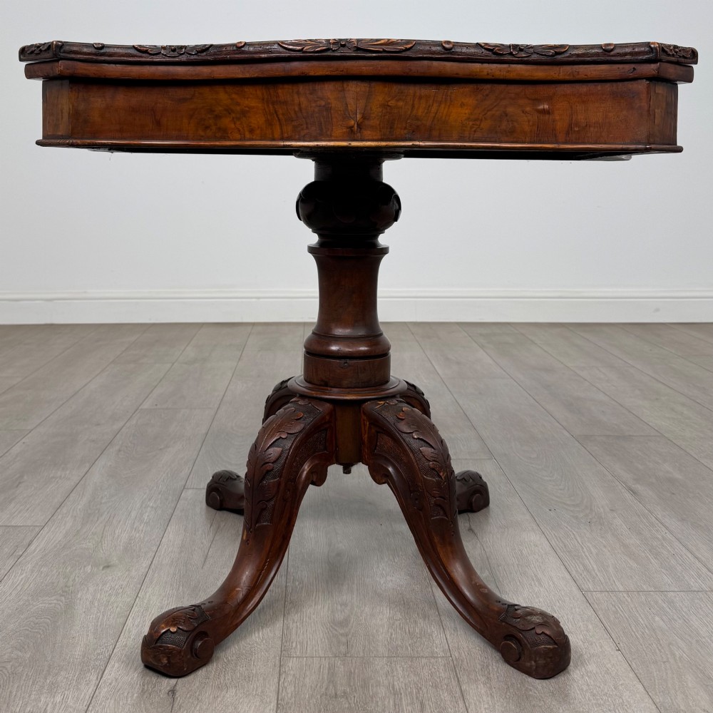 A 19th-century Victorian tea table in figured walnut, showcasing a carved rim, deep apron, turned pedestal, and four acanthus-carved scroll legs.