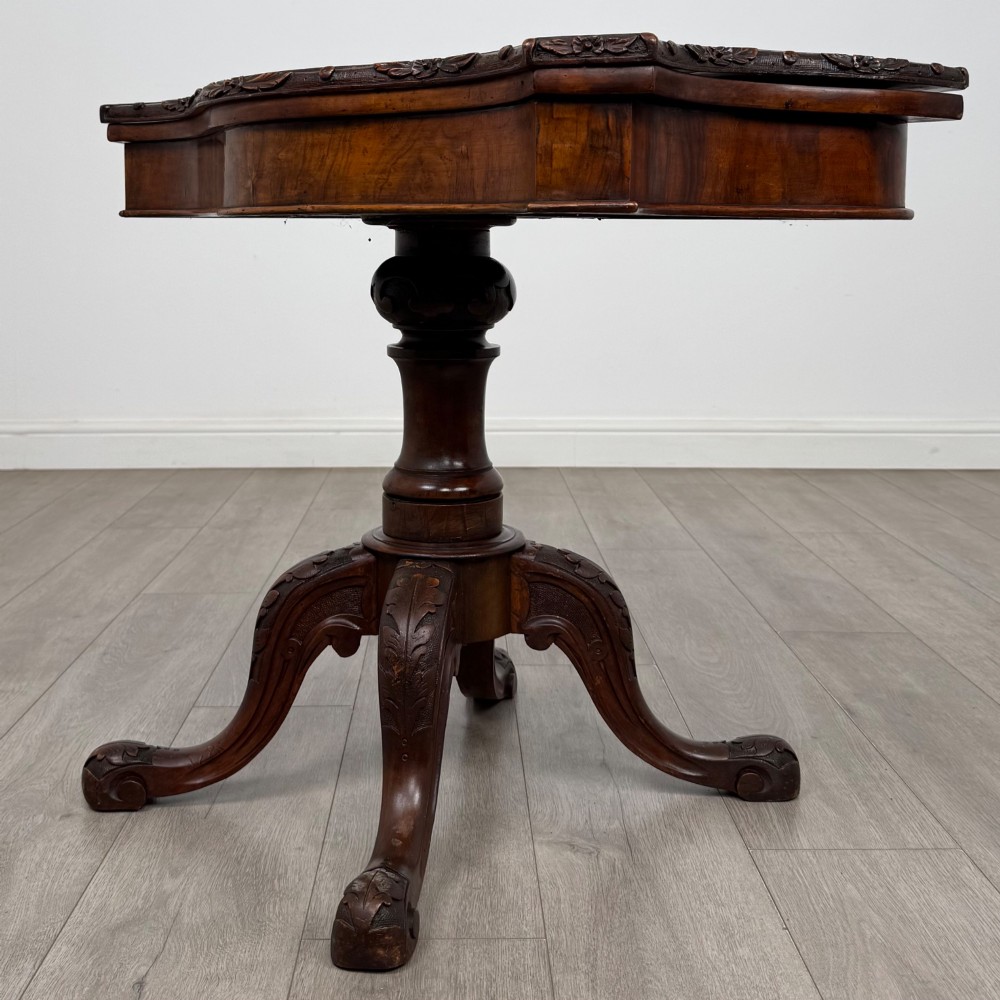 A 19th-century Victorian tea table in figured walnut, showcasing a carved rim, deep apron, turned pedestal, and four acanthus-carved scroll legs. View II