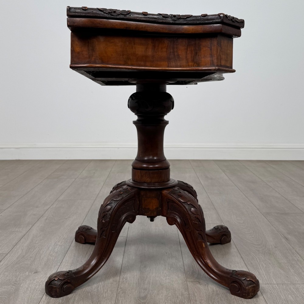 A 19th-century Victorian tea table in figured walnut, showcasing a carved rim, deep apron, turned pedestal, and four acanthus-carved scroll legs. View VII