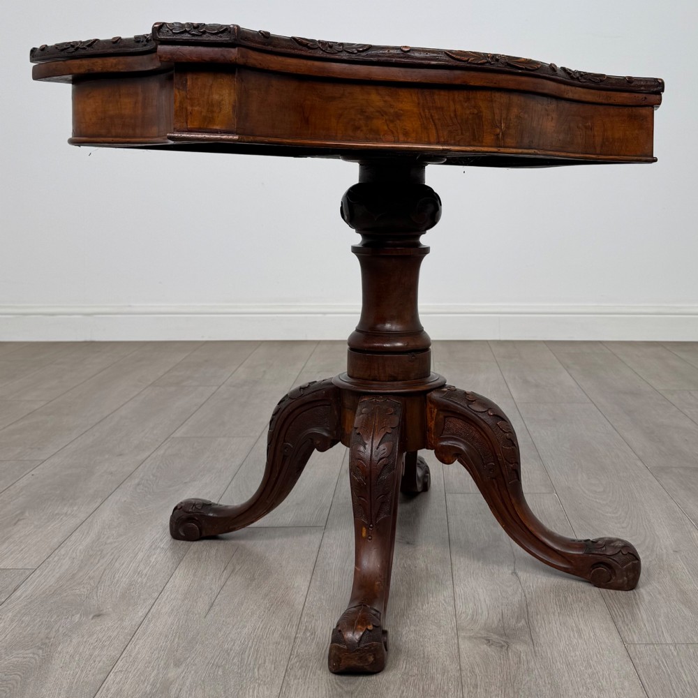 A 19th-century Victorian tea table in figured walnut, showcasing a carved rim, deep apron, turned pedestal, and four acanthus-carved scroll legs. View VIII