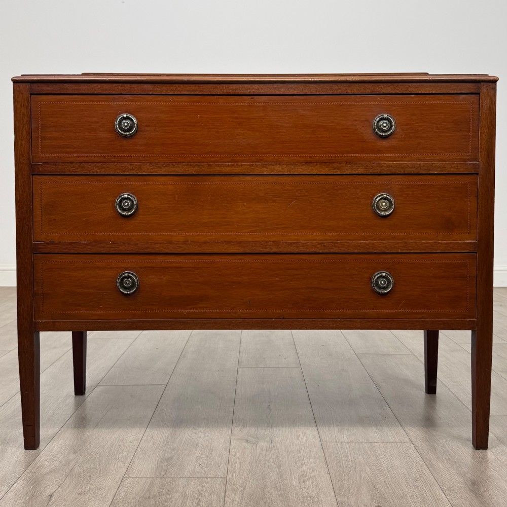 A 20th-century mahogany chest of drawers featuring three straight drawers with string inlay borders, brass ring handles, and square tapered legs.