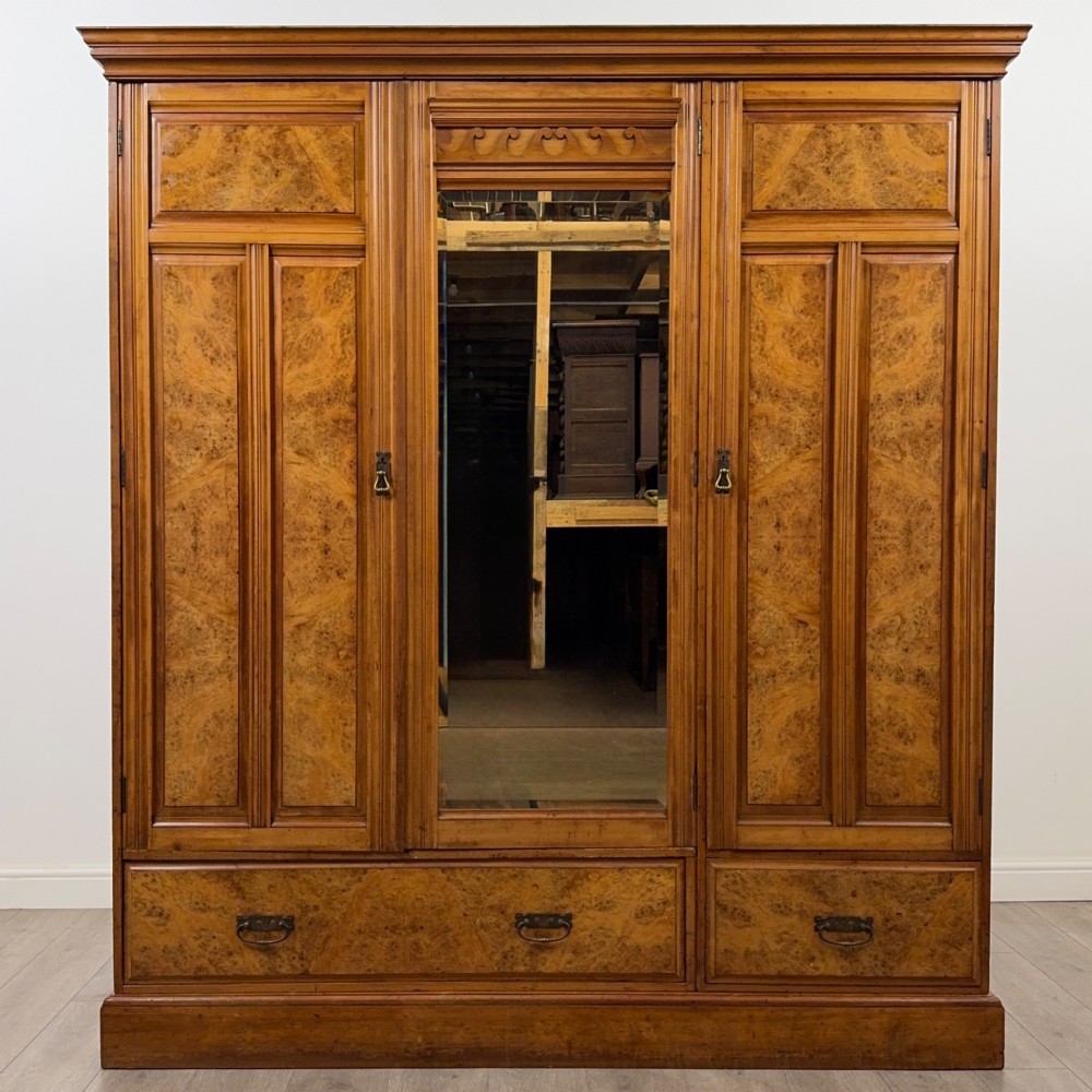 A large Art Deco burr walnut triple wardrobe featuring a central mirror door flanked by two panelled doors over base drawers.