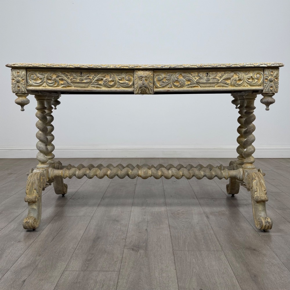 A 19th-century carved oak writing table with spiral barley-twist legs, foliage carving on the drawer frieze, and a weathered grey finish.