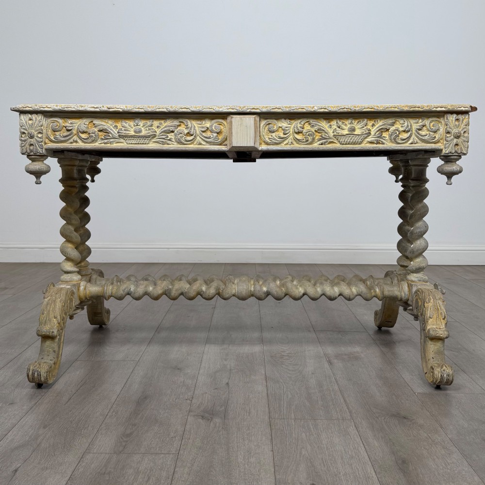 A 19th-century carved oak writing table with spiral barley-twist legs, foliage carving on the drawer frieze, and a weathered grey finish. View V