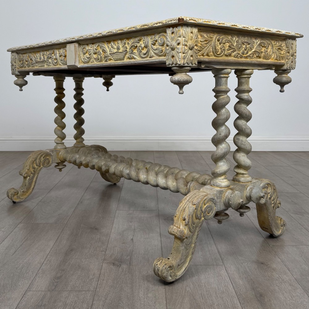A 19th-century carved oak writing table with spiral barley-twist legs, foliage carving on the drawer frieze, and a weathered grey finish. View VI
