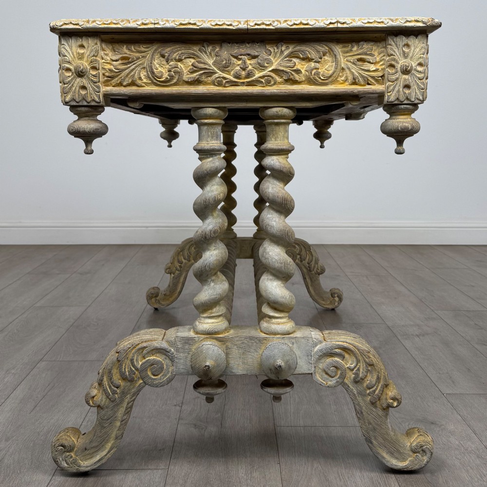 A 19th-century carved oak writing table with spiral barley-twist legs, foliage carving on the drawer frieze, and a weathered grey finish. View VII