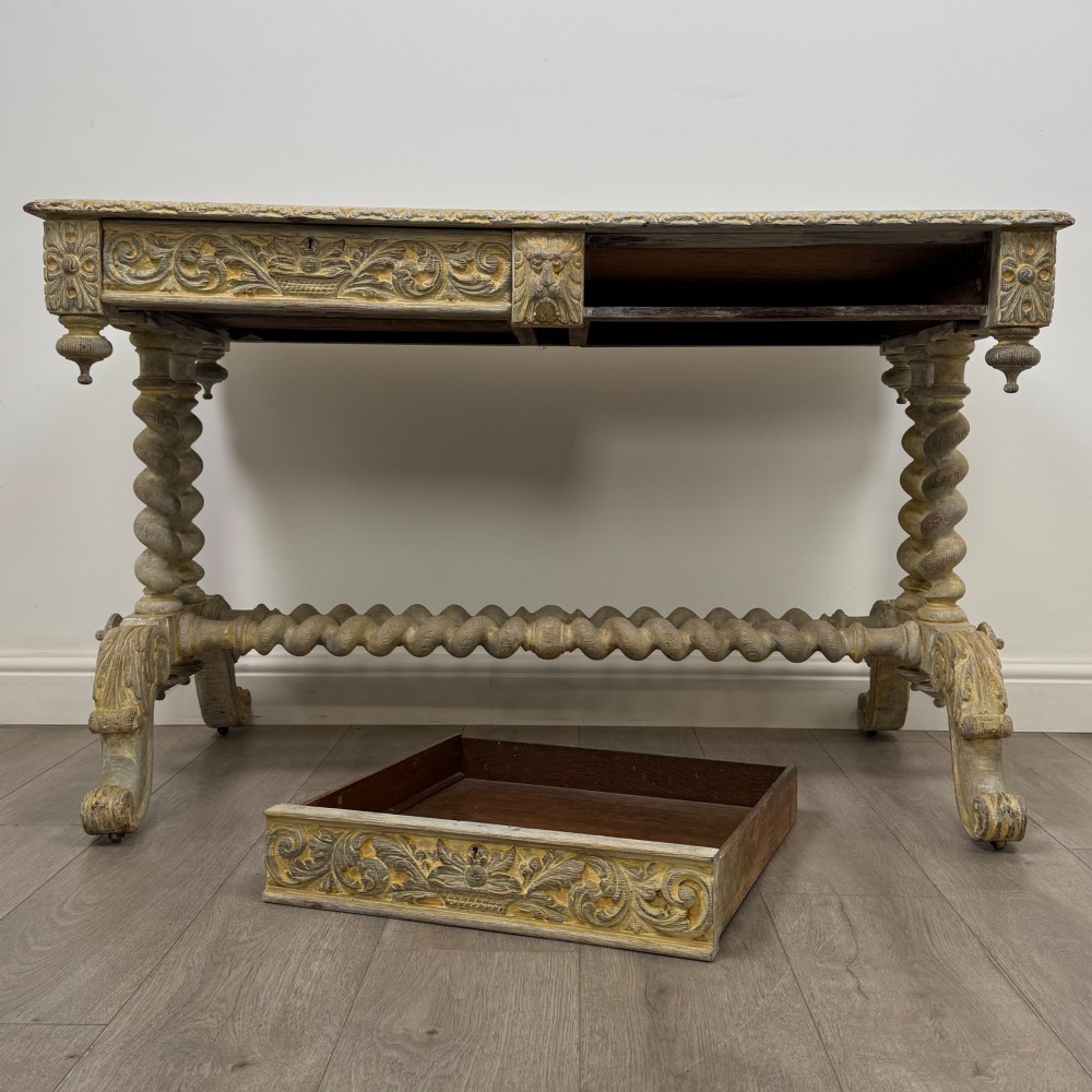 A 19th-century carved oak writing table with spiral barley-twist legs, foliage carving on the drawer frieze, and a weathered grey finish. View X