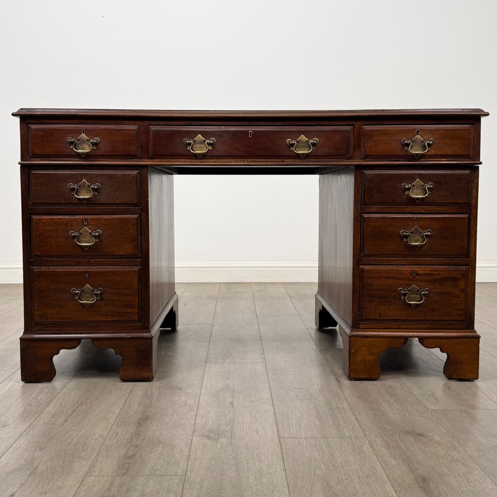 A 20th-century mahogany twin pedestal desk featuring nine drawers with brass drop handles and bracket feet.