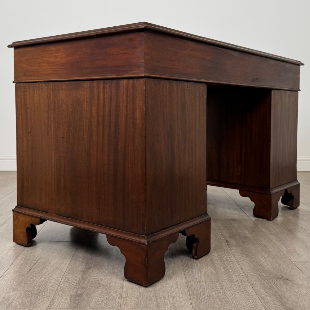 A 20th-century mahogany twin pedestal desk featuring nine drawers with brass drop handles and bracket feet. View IV