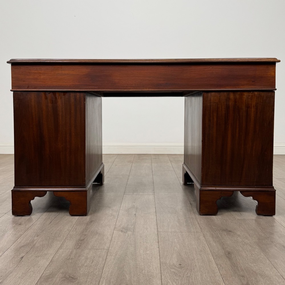 A 20th-century mahogany twin pedestal desk featuring nine drawers with brass drop handles and bracket feet. View V