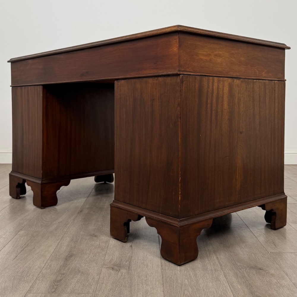 A 20th-century mahogany twin pedestal desk featuring nine drawers with brass drop handles and bracket feet. View VI